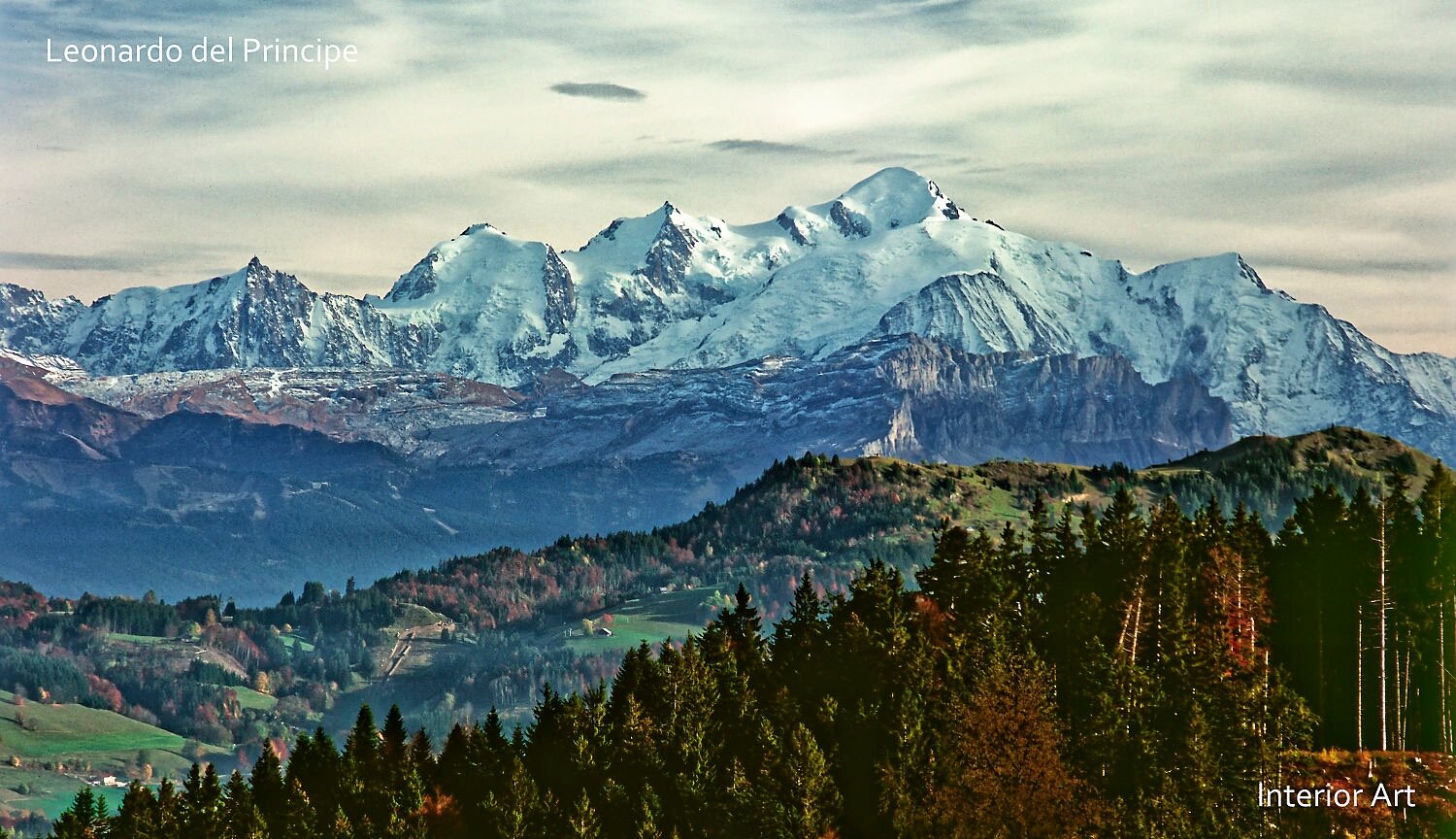HBSD04 Snow-capped Mont-Blanc tower over rolling hills and dense forests under a cloudy sky. The landscape conveys tranquility and grandeur.