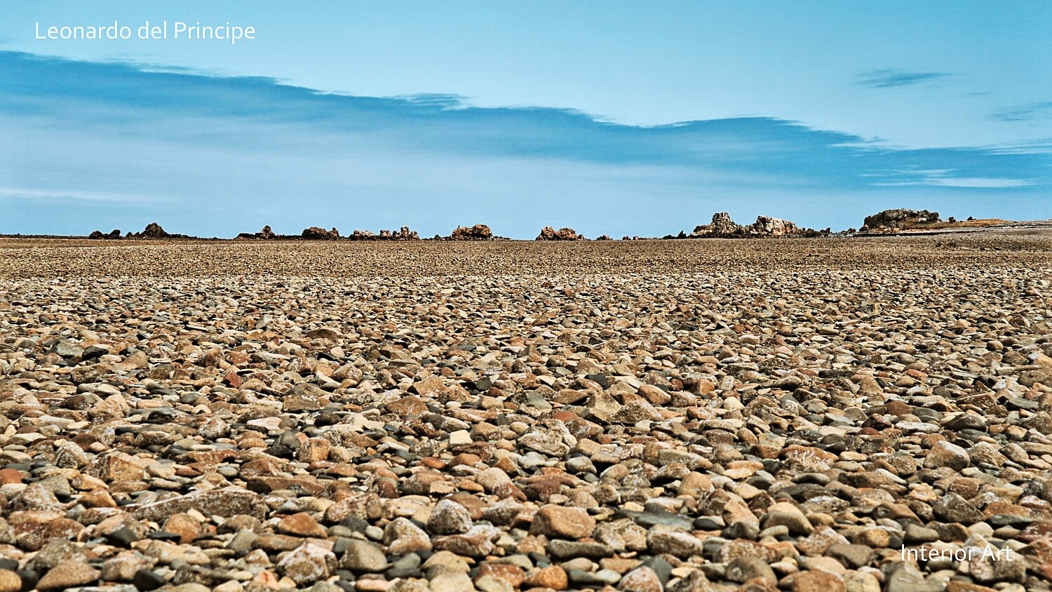 MORG05 A vast expanse of smooth, round stones stretches into the distance under a clear blue sky. Rocky formations outline the horizon, conveying tranquility.