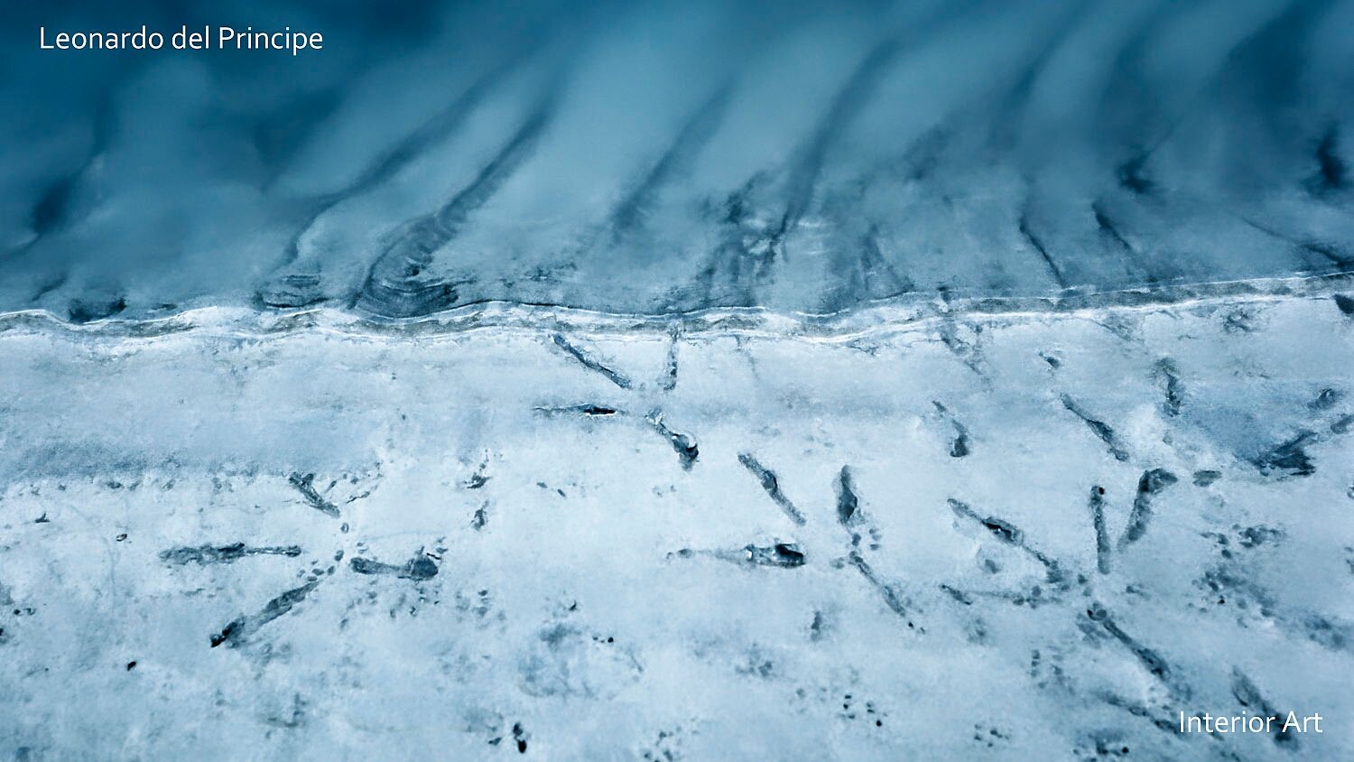 PARI05 Aerial view of icy blue creek with dark trails resembling brush strokes, conveying a serene and abstract winter scene.